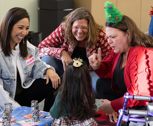 Three adults interacting playfully with a young child during a holiday-themed activity